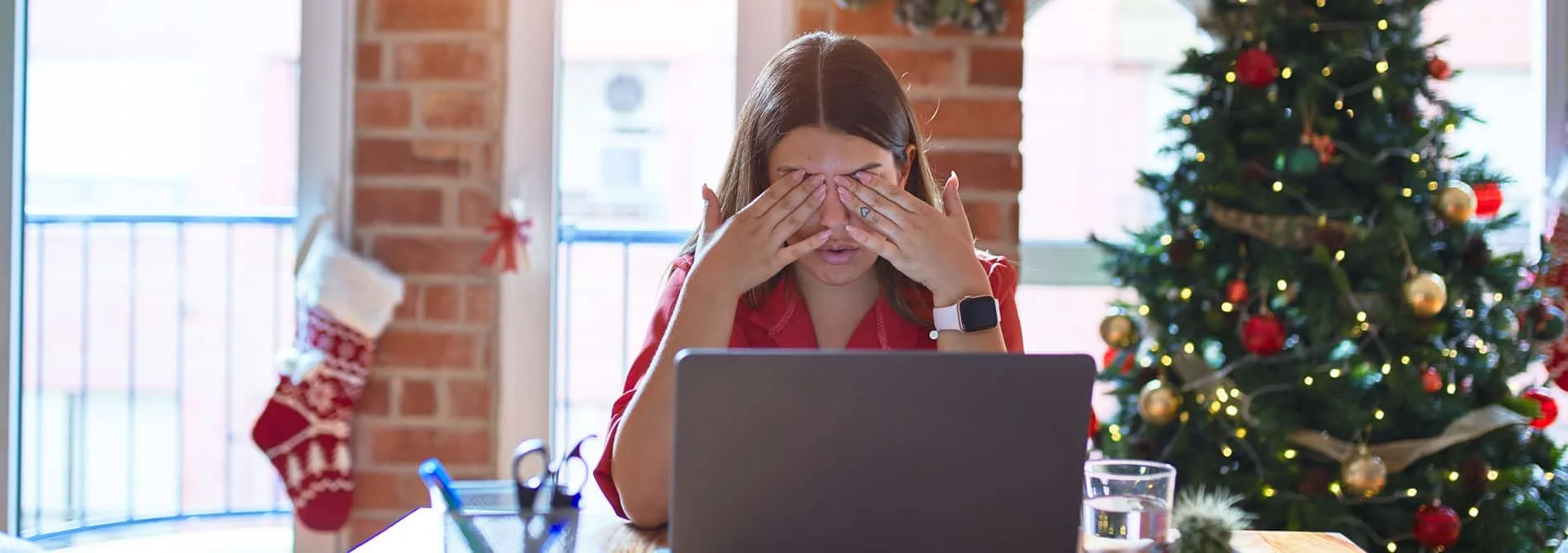 Woman stressed out sitting a table with Christmas tree in background.