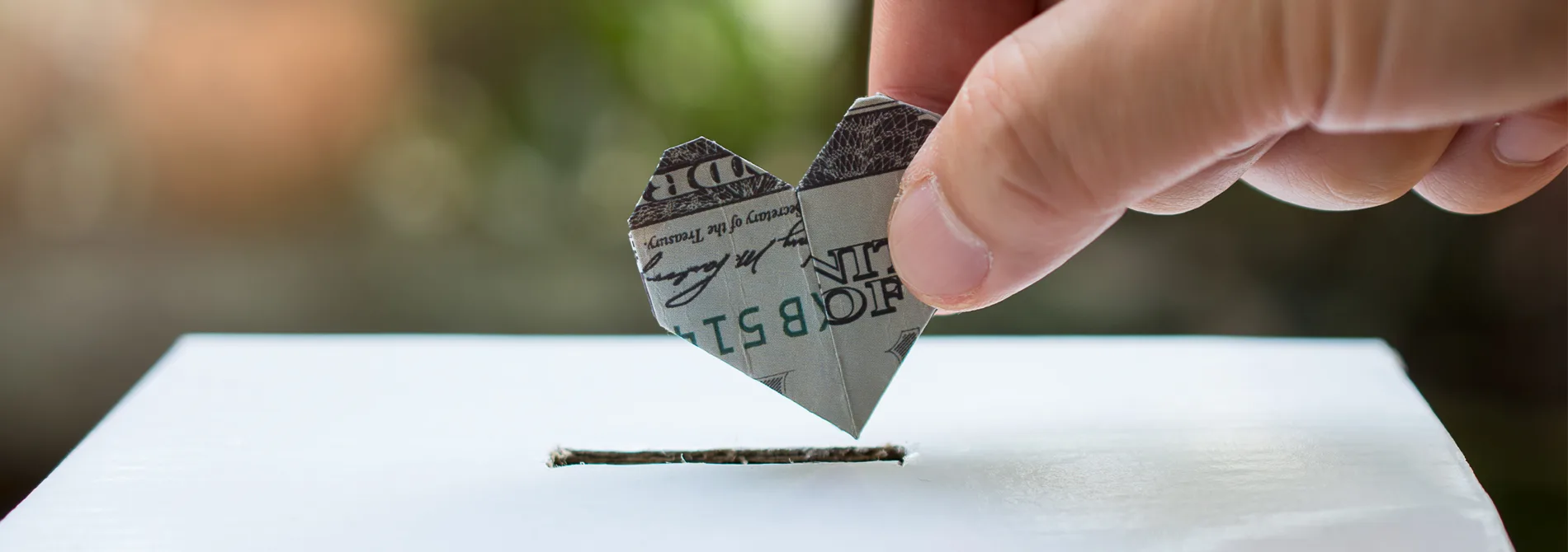 image of money folded into heart being put in donation box.